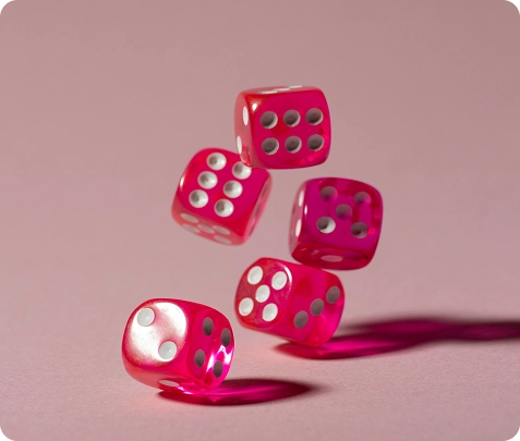 Zes roze dobbelstenen met witte stippen zijn vastgelegd terwijl ze door de lucht zweven, tegen een zachtroze achtergrond. De compositie is dynamisch en levendig en straalt beweging uit.